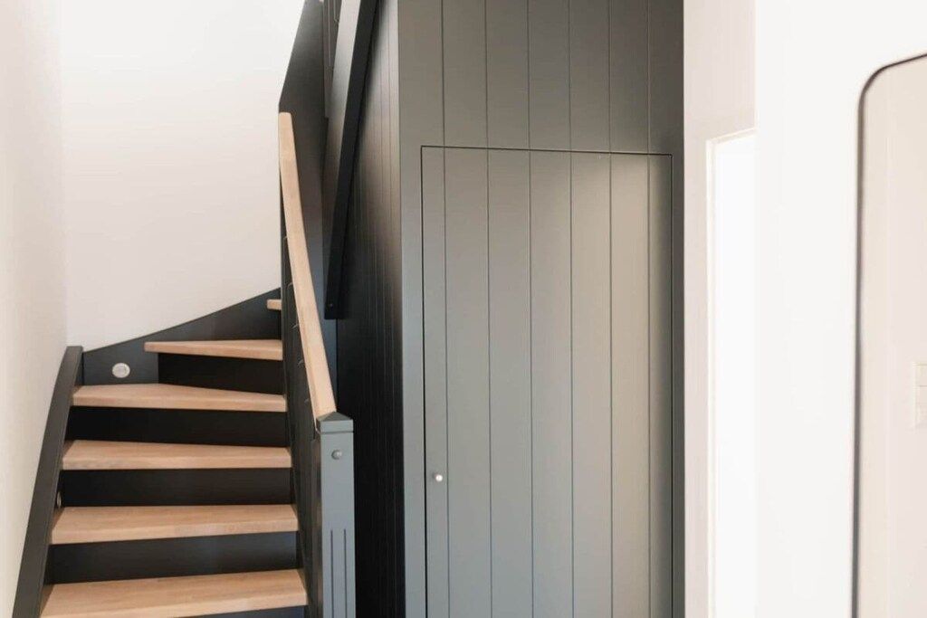 A staircase with wooden steps and a black railing leading to a grey door.
