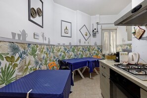 A kitchen with two tables, a gas stove, and decorative wall art. - Holiday Home 'San Pietro House' with Balcony, Wi-Fi and Air Conditioning (Roma)