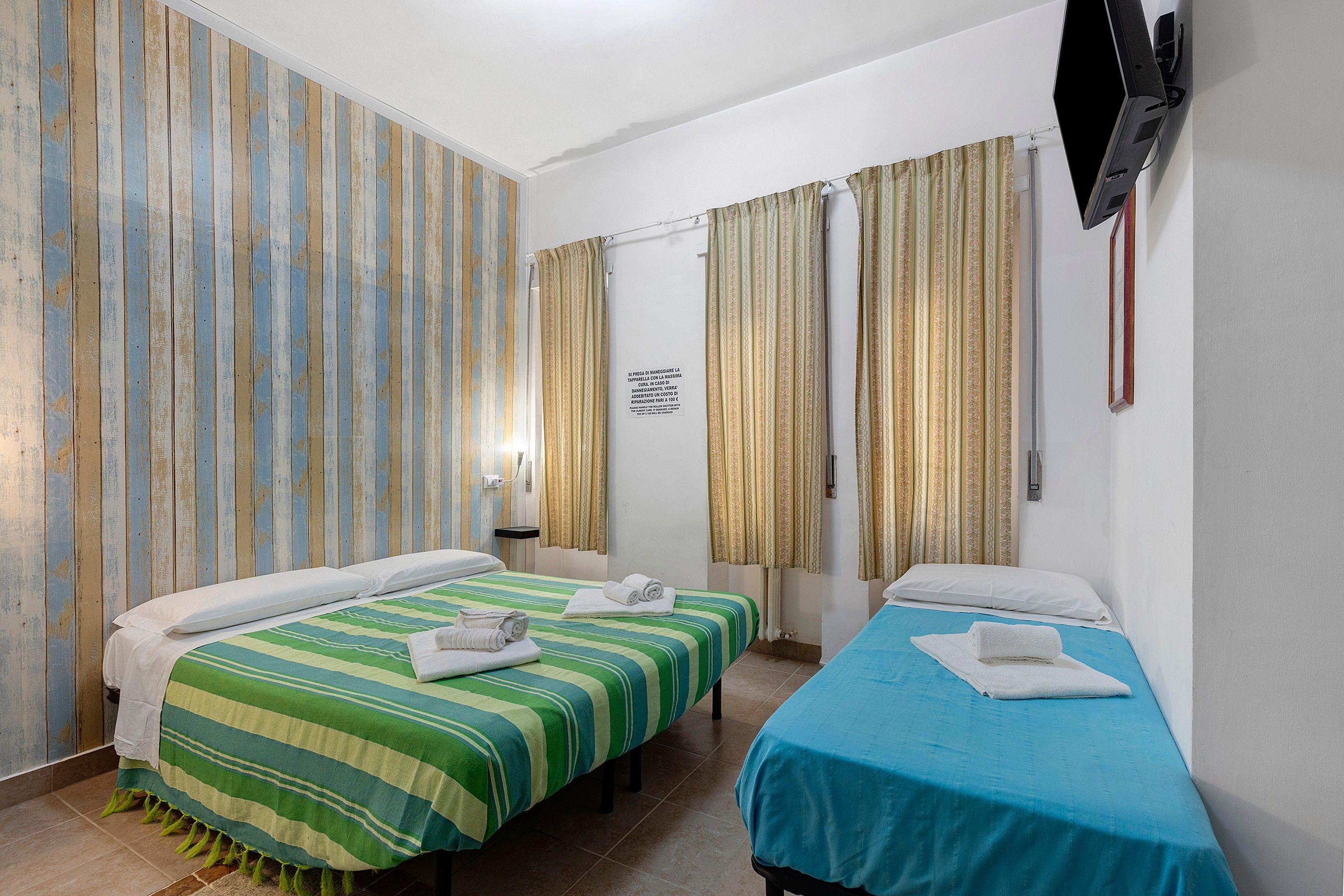 Une chambre d’hôtel avec deux lits simples, un téléviseur fixé au mur et des rideaux à rayures.