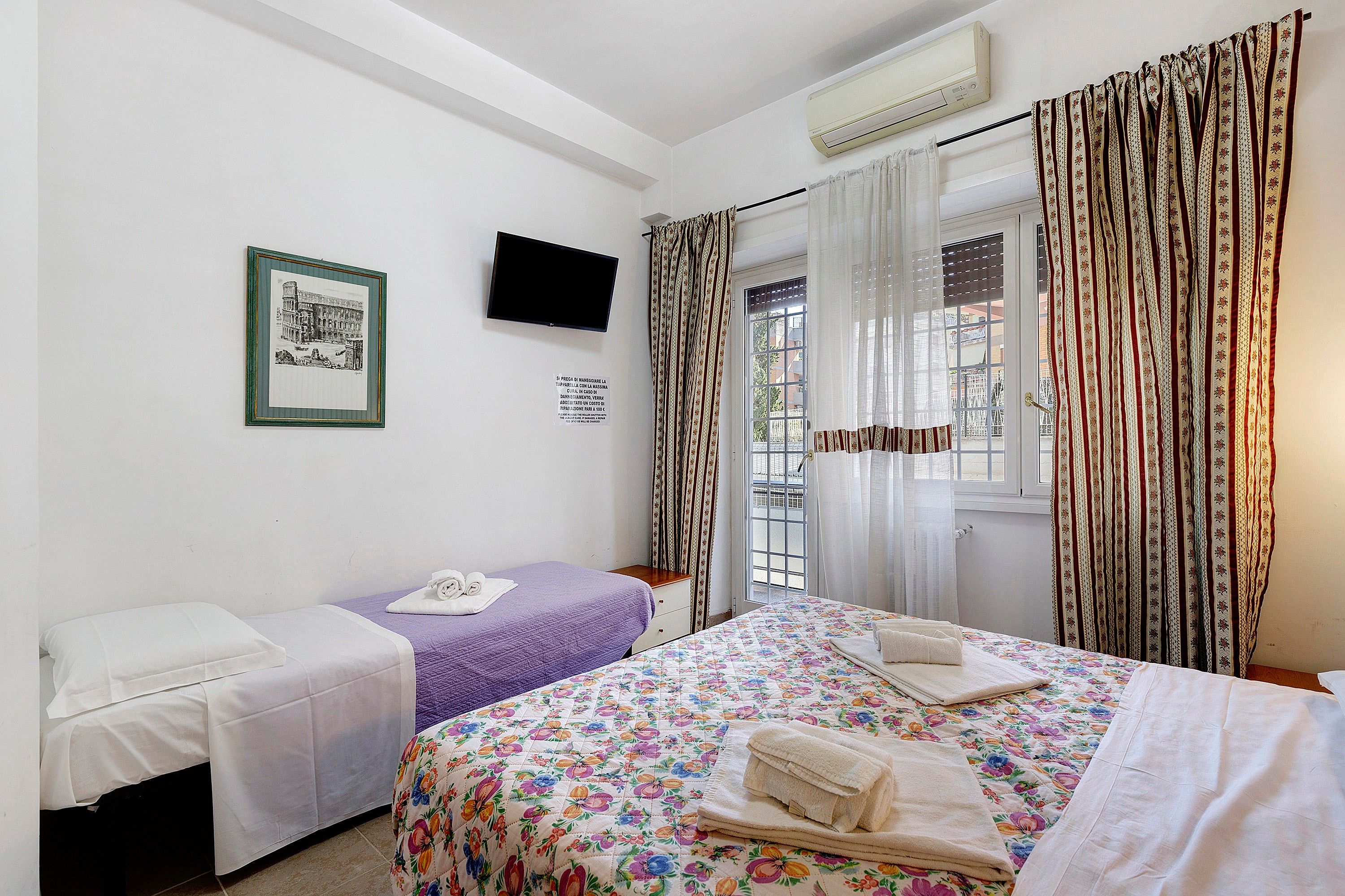 Une chambre d’hôtel avec deux lits, une télévision, un appareil de climatisation et une fenêtre avec des rideaux.
