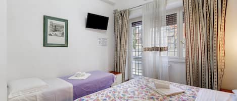 Une chambre d’hôtel avec deux lits, une télévision, un appareil de climatisation et une fenêtre avec des rideaux.