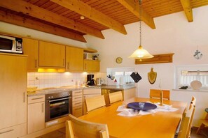 A kitchen with wooden cabinets, a stove, and a dining table with chairs. - Holiday home with 3 bedrooms (Neßmersiel)
