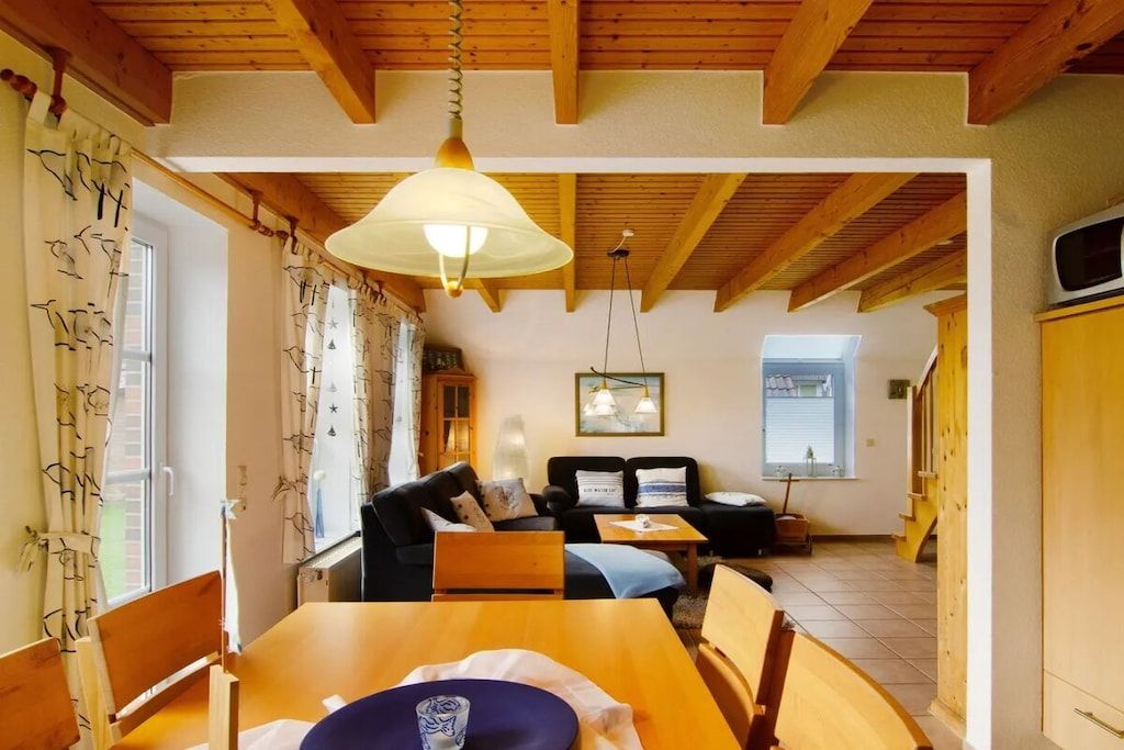 Una habitación acogedora con techo de madera, una mesa de comedor con sillas, un sofá y una ventana con cortinas.