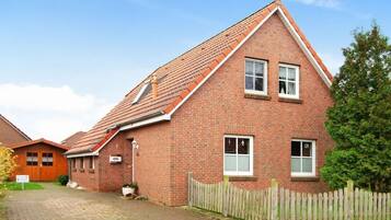 A two-story brick house with a sloped roof, a wooden fence, and a paved driveway.