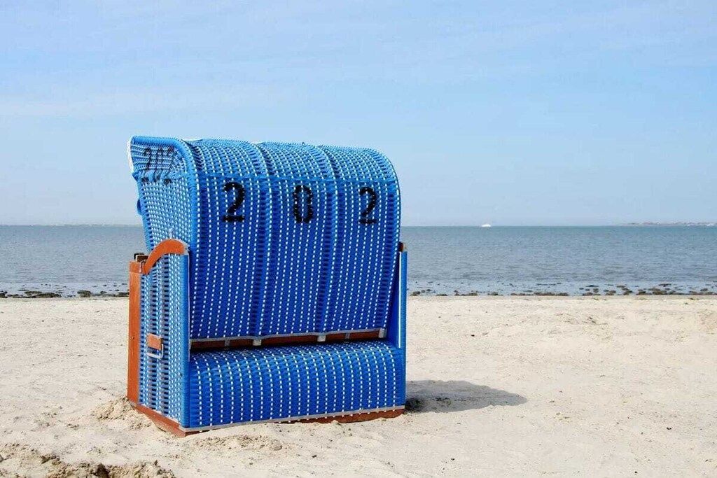 Una silla de playa azul con los números '2022' sobre arena, con el mar al fondo.