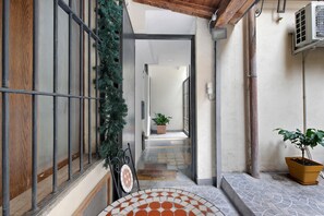 A narrow corridor with a tiled floor, a potted plant, a metal gate, and a door leading to a room. - Apartment 'Colosseum From Flavio Rome Historic' with Private Garden, Wi-Fi and Air Conditioning (Roma)