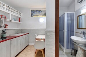 Ein kleines Badezimmer mit Dusche, Waschbecken und einem Tisch mit Stuhl.