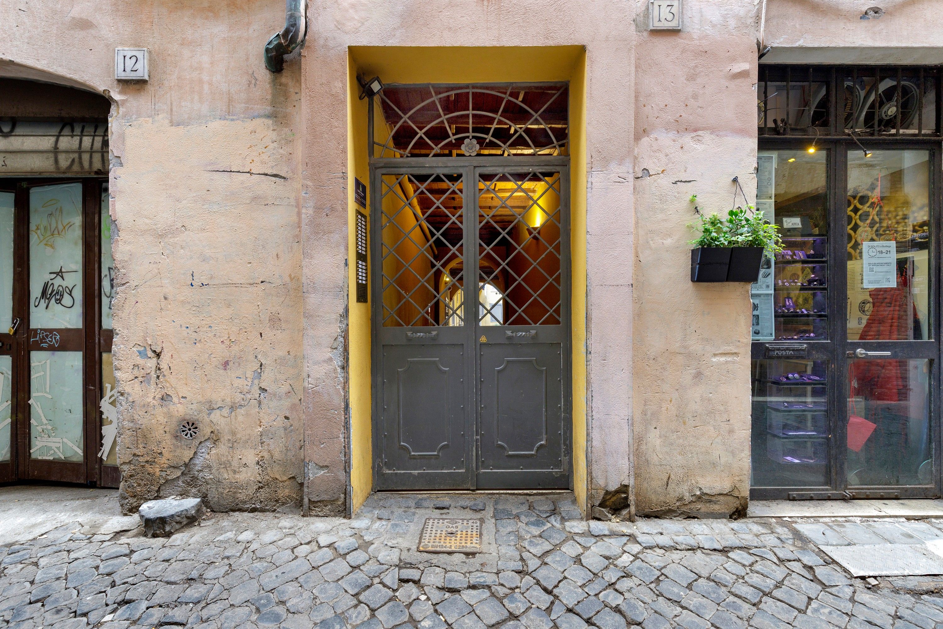 A building entrance with a metal gate, a cobblestone pavement, and a shop window with items on display.
