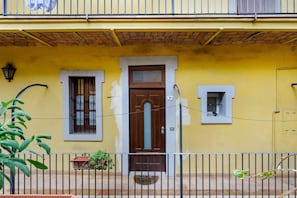 A yellow building with a brown door, two windows, and a small balcony with a potted plant. - Apartment 'Stay in The Heart Of Rome' with Wi-Fi and Air Conditioning (Roma)