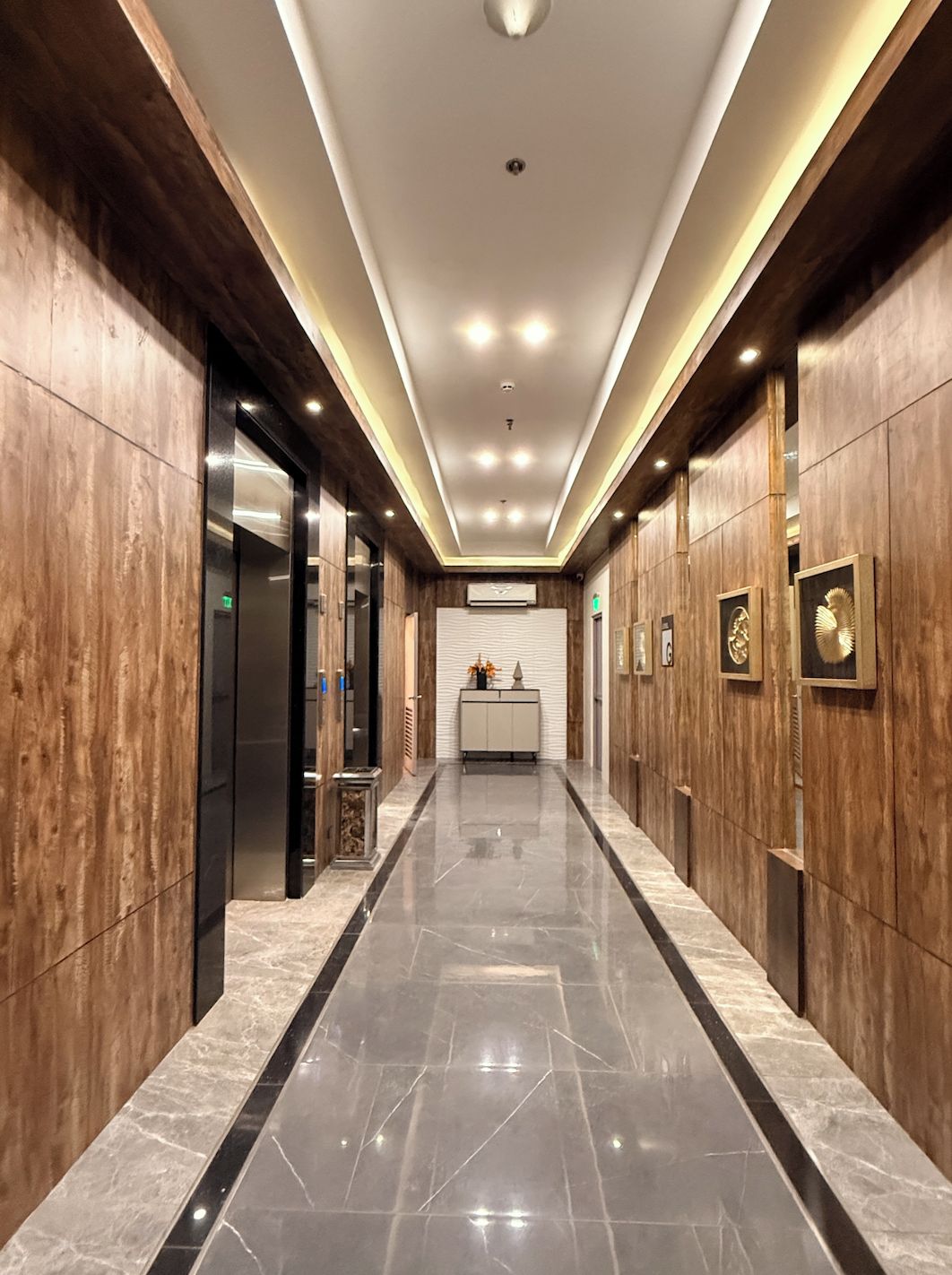 A hallway with wooden paneling, a marble floor, and a central reception desk with a white backdrop.
