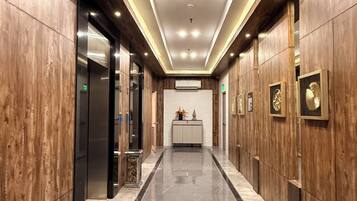 A hallway with wooden paneling, a marble floor, and a central reception desk with a white backdrop.