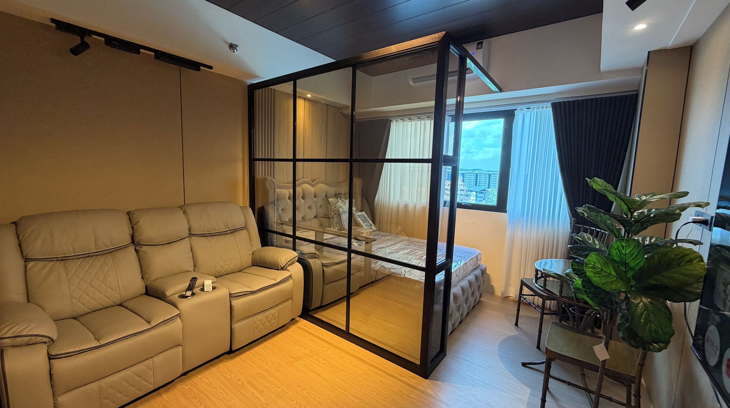 Un dormitorio moderno con sofá, cama, separador de vidrio y vistas de la ciudad.