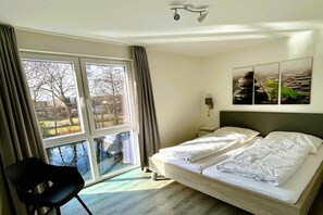 A hotel room with a bed, a chair, a window with curtains, and a wall-mounted lamp. - House No. 33, Holiday Home Deichgraf (Wangerland)
