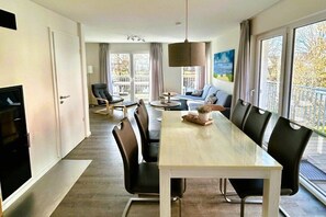 A modern hotel room with a dining area, a sofa, a TV, and a balcony with a view. - House No. 33, Holiday Home Deichgraf (Wangerland)