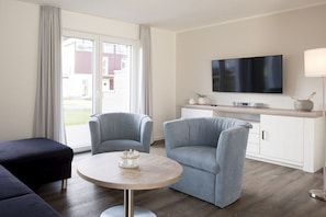 Ein modernes Wohnzimmer mit einem runden Tisch, zwei Sesseln, einer Couch, einem Flachbildfernseher und einem Schrank.