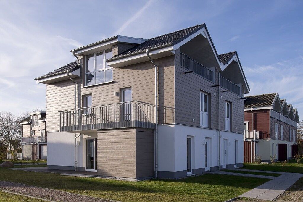 A modern two-story residential building with a balcony, a garage, and a well-maintained lawn.