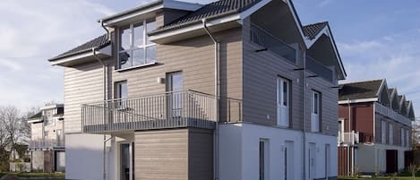 A modern two-story residential building with a balcony, a garage, and a well-maintained lawn.