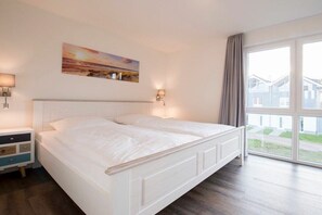 Ein Doppelbett mit Kopfteil, Nachttischlampen, einem Beistelltisch und einem großen Fenster mit Vorhängen.