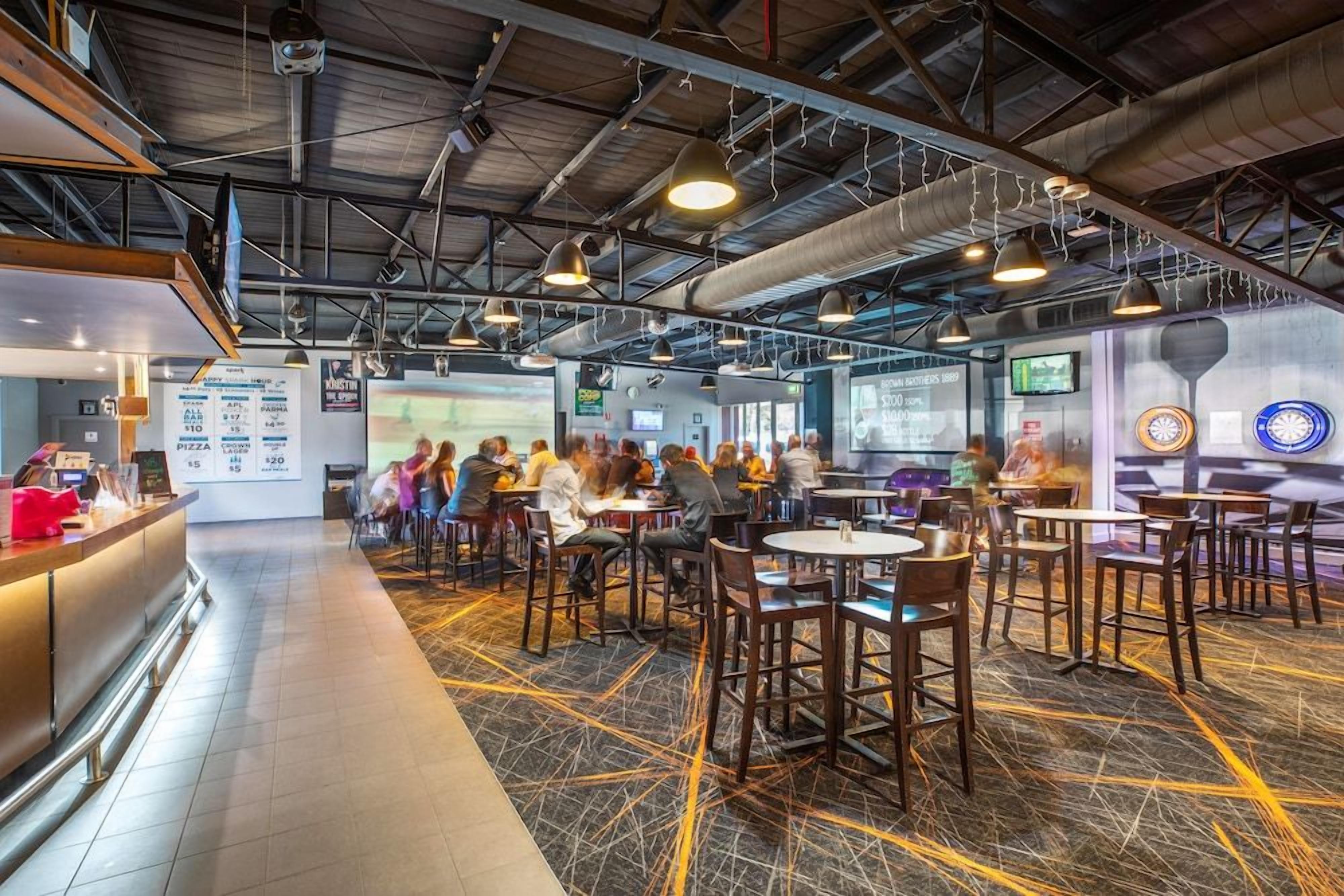 A restaurant with a high ceiling, exposed ductwork, and pendant lighting. There are multiple tables and chairs arranged for dining.