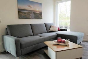 Ein modernes Wohnzimmer mit einem grauen Sofa, einem Holztisch und einem Gemälde einer Küstenlandschaft.