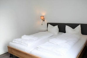 Ein Doppelbett mit weißen Bettwäsche, einem Holz-Kopfteil und einer Wandleuchte.