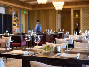 Un ambiente de restaurante con mesas preparadas para comer, incluyendo copas de vino, cubiertos y servilletas.