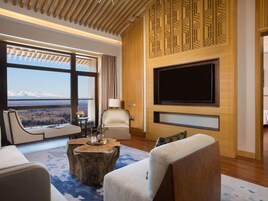 Una sala de estar moderna con un televisor grande, asientos cómodos, vistas a montañas y una pared de acento de madera.