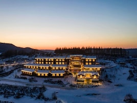Un gran lodge de varios pisos con distribución simétrica, rodeado por terreno cubierto de nieve y un bosque de fondo.