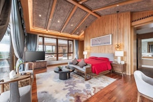 Una habitación de hotel moderna con una cama grande, televisión, sofá y zona de comedor.