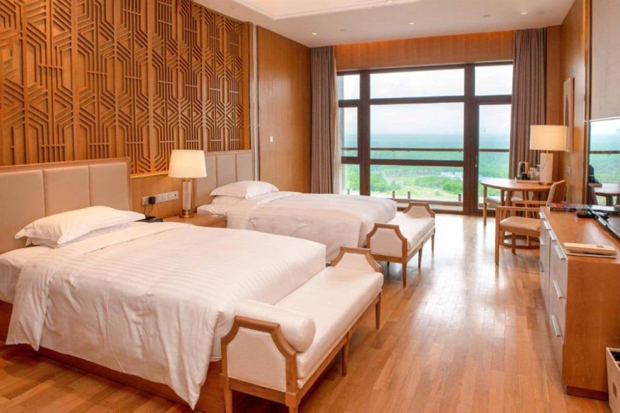 A hotel room with two beds, a desk, and a view of the landscape.