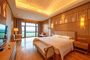 A hotel room with a large bed, a desk, a chair, a TV, and a view of the outdoors.