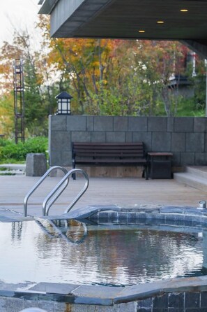 Una piscina exterior con escaleras de metal, un muro de piedra, un banco de madera y un farol.