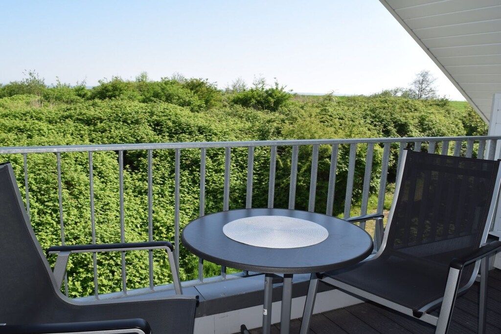 Un balcon avec une table et des chaises, donnant sur un paysage verdoyant et luxuriant.