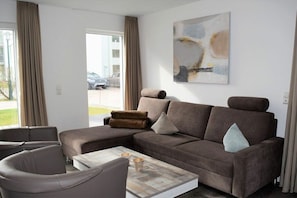 A modern living room with a sectional sofa, a coffee table, and a large abstract painting on the wall. - House No. 23, Holiday Home Deichgraf (Wangerland)