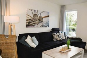 A modern living room with a black sofa, a wooden coffee table, and a large window with a view. - House No. 40, Holiday Home Deichgraf (Wangerland)