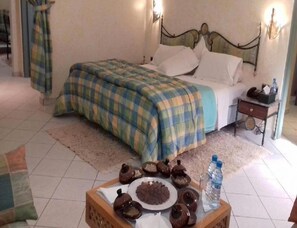 A hotel room with a bed, a bedside table, a nightstand, a tray with food, and a water bottle. - Belere (Aarab Sebbah Ziz)