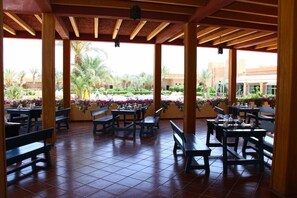 An outdoor patio area with wooden benches and tables, surrounded by potted plants and flowers. - Belere (Aarab Sebbah Ziz)