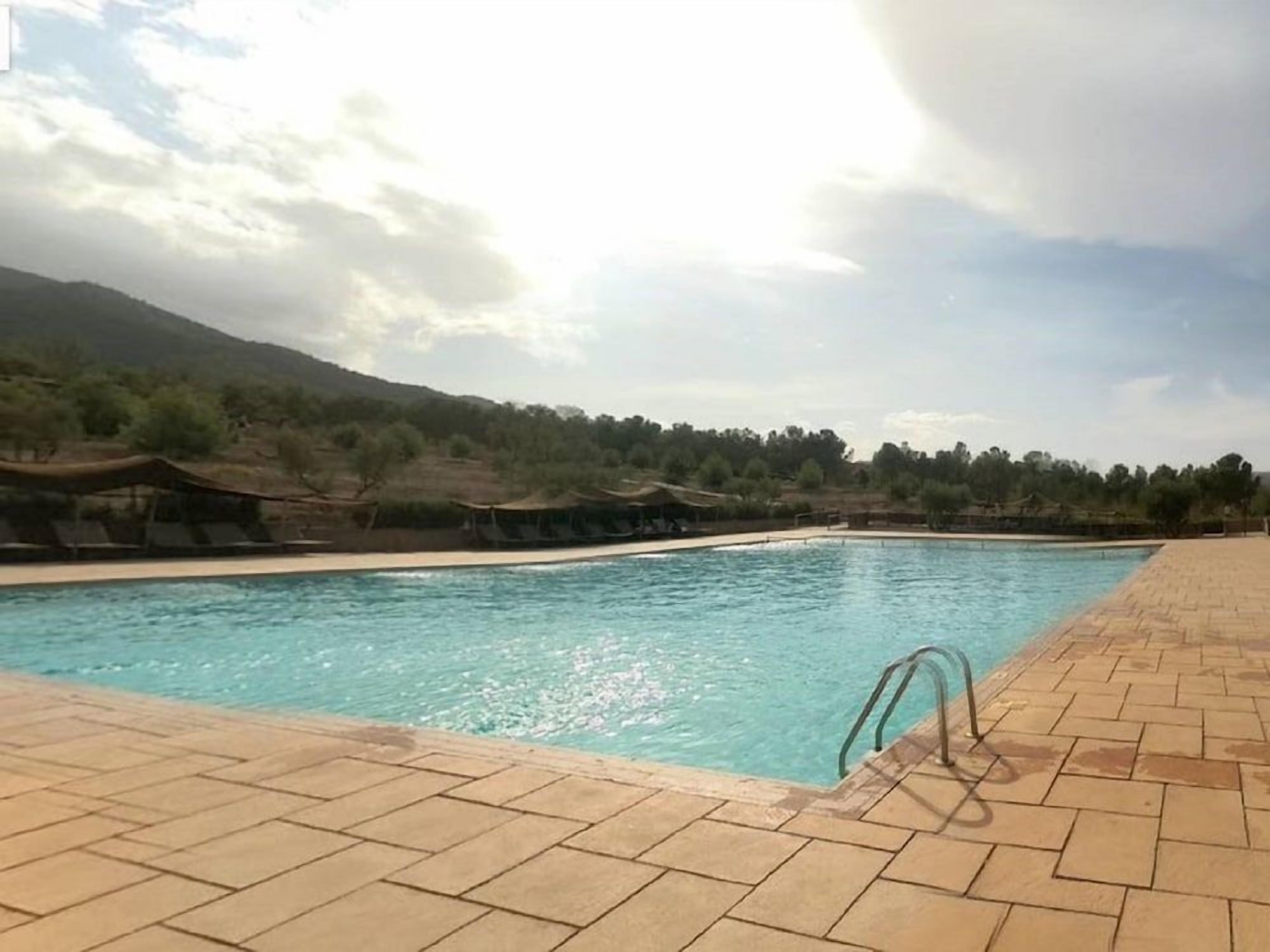 Une piscine dotée d’une terrasse carrelée, entourée d’un paysage vallonné.
