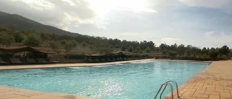 A swimming pool with a tiled deck, surrounded by a hilly landscape.