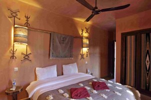 Habitación de hotel con cama, dos lámparas fijadas a la pared, ventilador de techo y puerta de diseño tradicional.