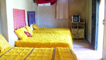 Une chambre avec deux lits recouverts de draps jaunes, un téléviseur posé sur un meuble en bois et une porte donnant sur l’extérieur.