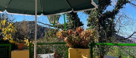 Área externa com mesas, cadeiras e um guarda-sol verde.