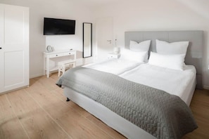 Une chambre à coucher comprenant un lit, des tables de chevet, un bureau, une chaise, un téléviseur et une porte.