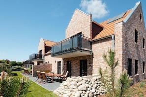 Ein modernes Backsteinhhaus mit Balkon, Sitzgelegenheit im Freien und einer Steinmauer.
