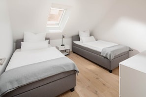 Quarto moderno com duas camas, um claraboia e mesa de cabeceira com abajur.
