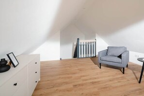 Quarto moderno com piso de madeira, uma poltrona cinza, penteadeira branca e escada para um andar superior.