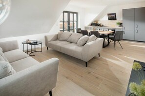 Ein moderner Loft-Wohnraum mit einer Couch, einem Esstisch, Stühlen und einer Küchenzeile.