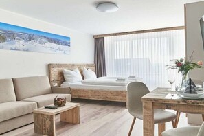 A hotel room with a bed, a sofa, a dining table, and a painting of a snowy landscape. - Holiday apartment 605 (Winterberg)