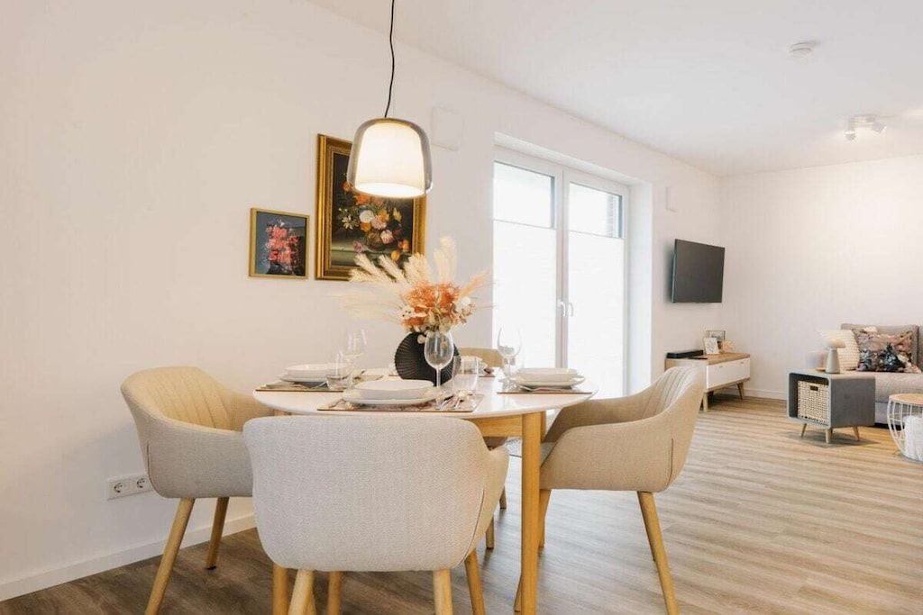 A dining area with a round table, four chairs, a vase with flowers, and a painting on the wall.