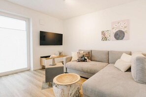 Ein modernes Wohnzimmer mit einer Couch, einem flachbildfernseher an der Wand und einem kleinen Beistelltisch.